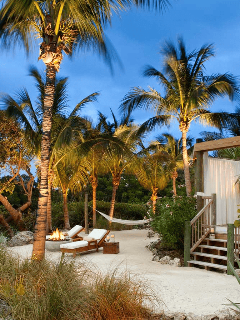 Tropical beach relaxation with palm trees, sun loungers, and hammock at sunset.