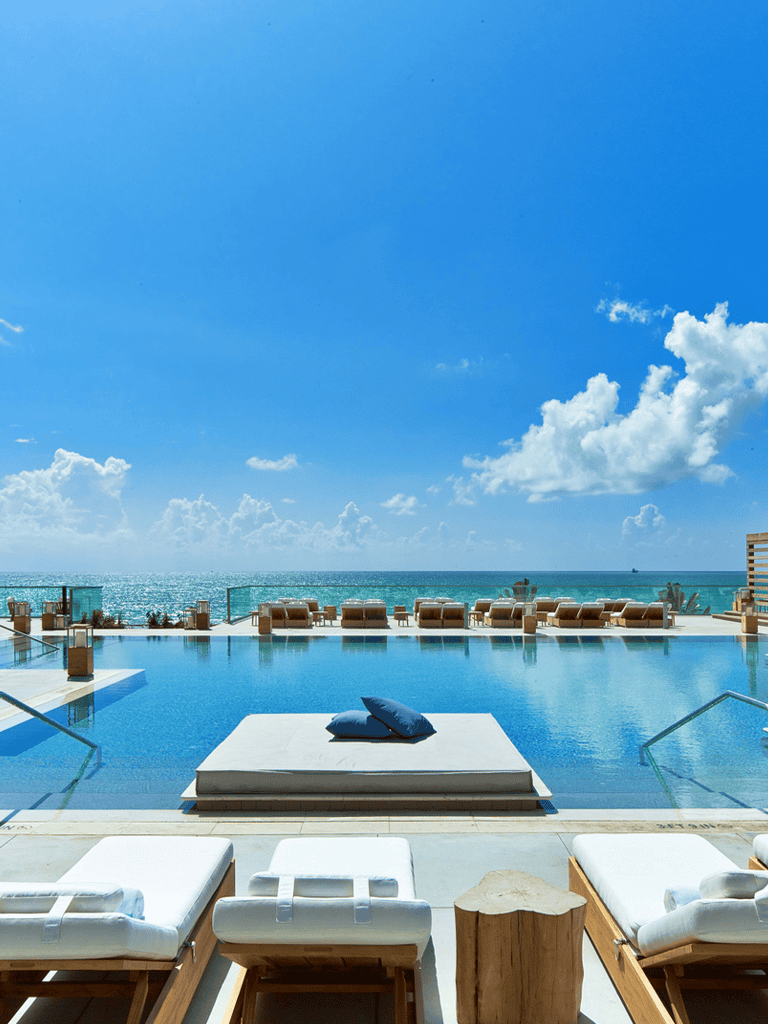 Luxurious infinity pool overlooking ocean with sunny sky and lounge chairs, perfect for relaxation.