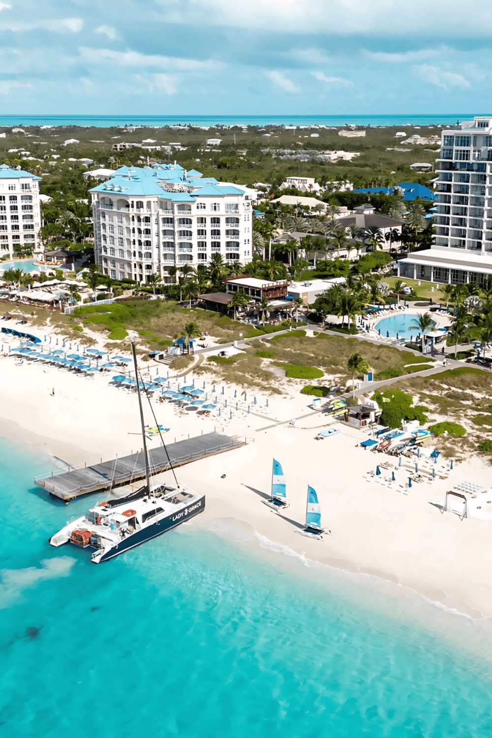Luxurious beachfront resort with pools and sailboats on white sandy beach.