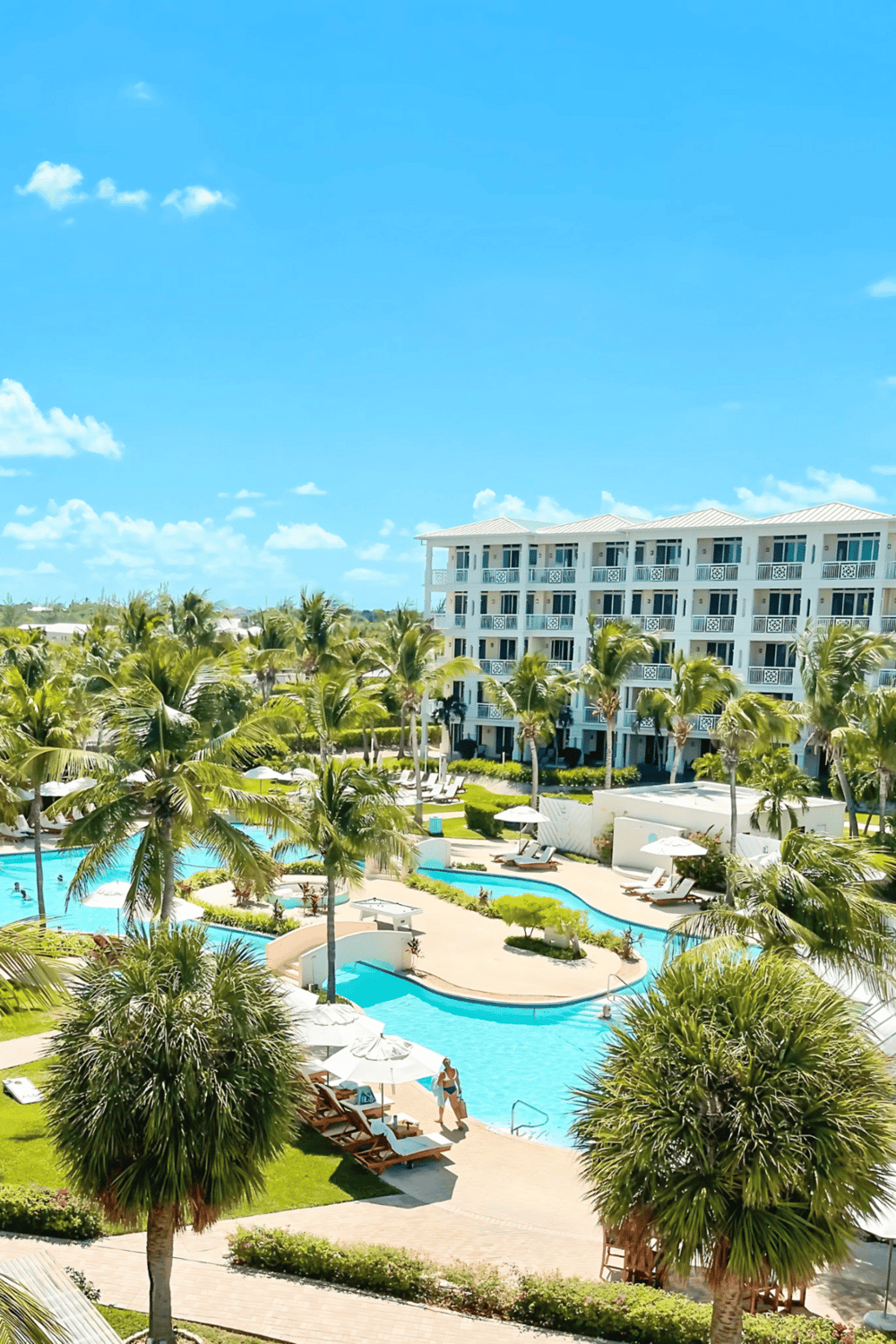 Luxurious tropical resort pool with palm trees and modern hotel buildings in the background.