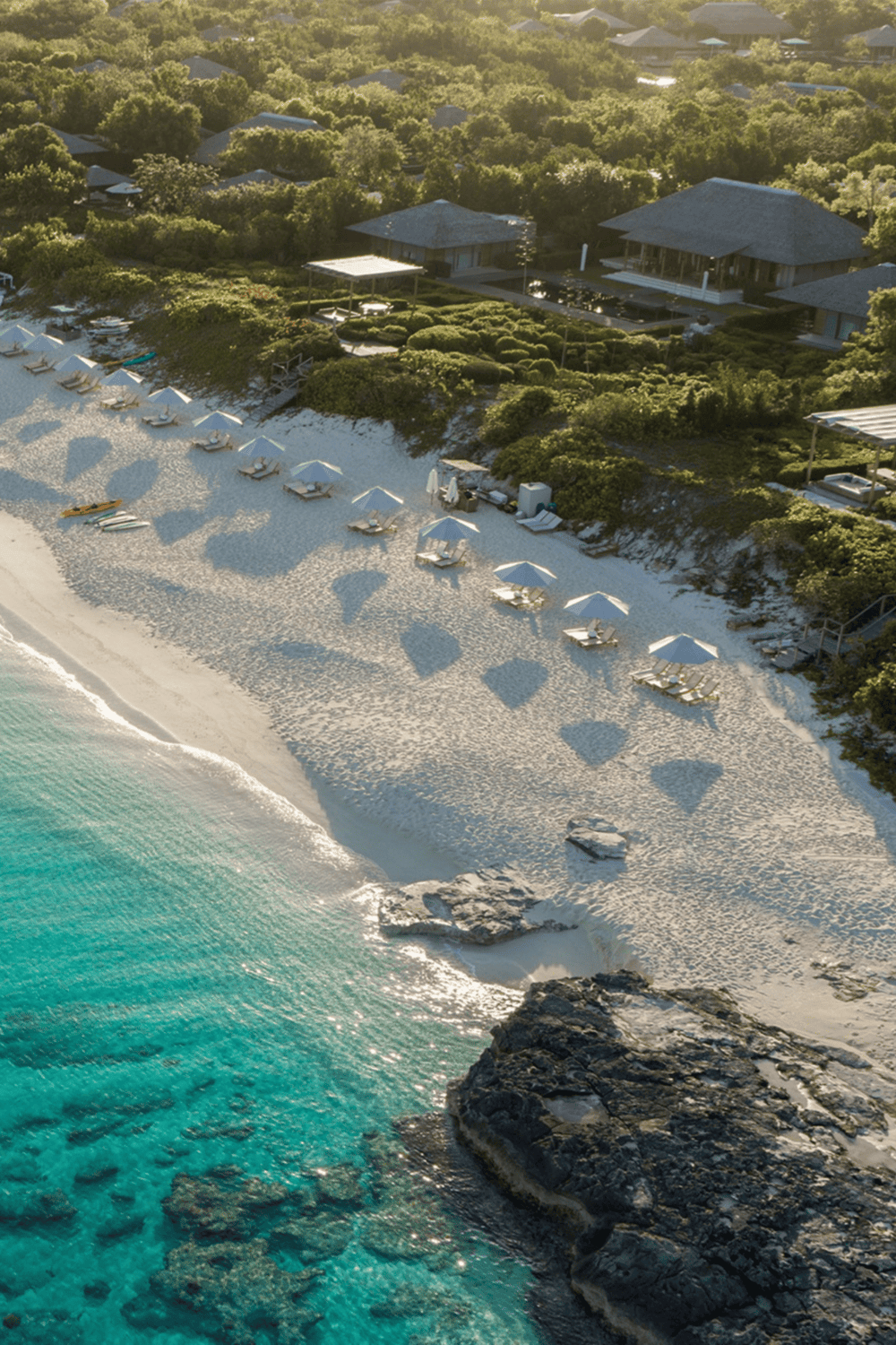 Lush beachfront resort with white sandy beach, umbrellas, and turquoise water.