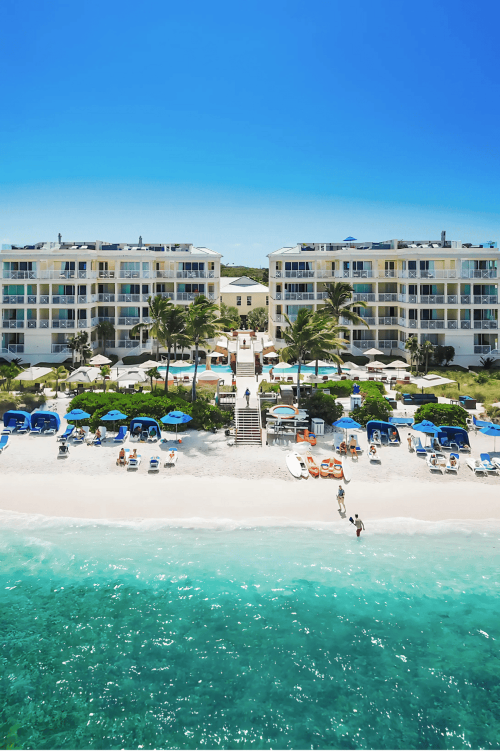 1. Modern beachfront resort with pools and loungers on white sandy beach under blue sky.