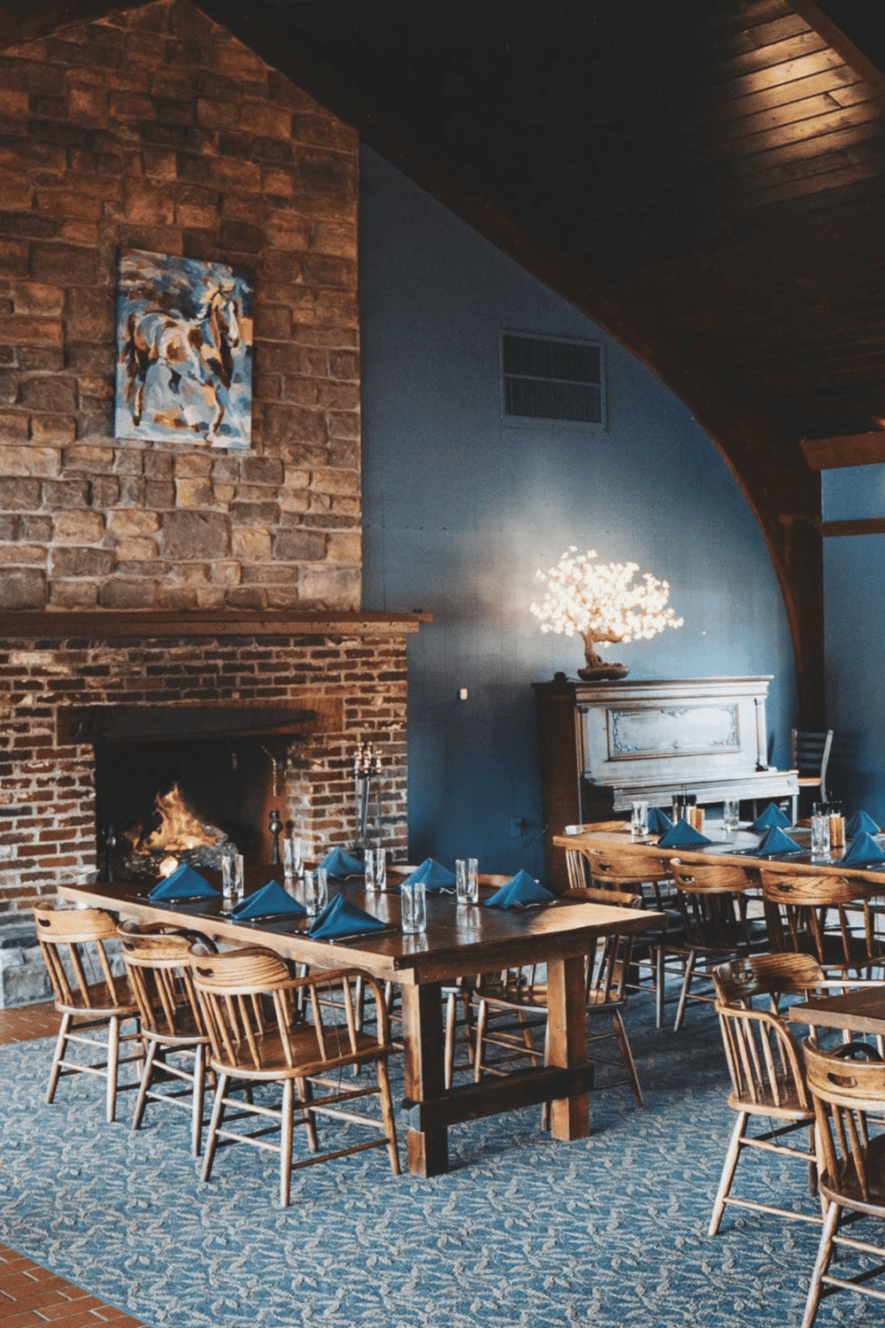 Cozy restaurant interior with a brick fireplace, blue walls, and wooden furniture, perfect for an inviting dining experience.