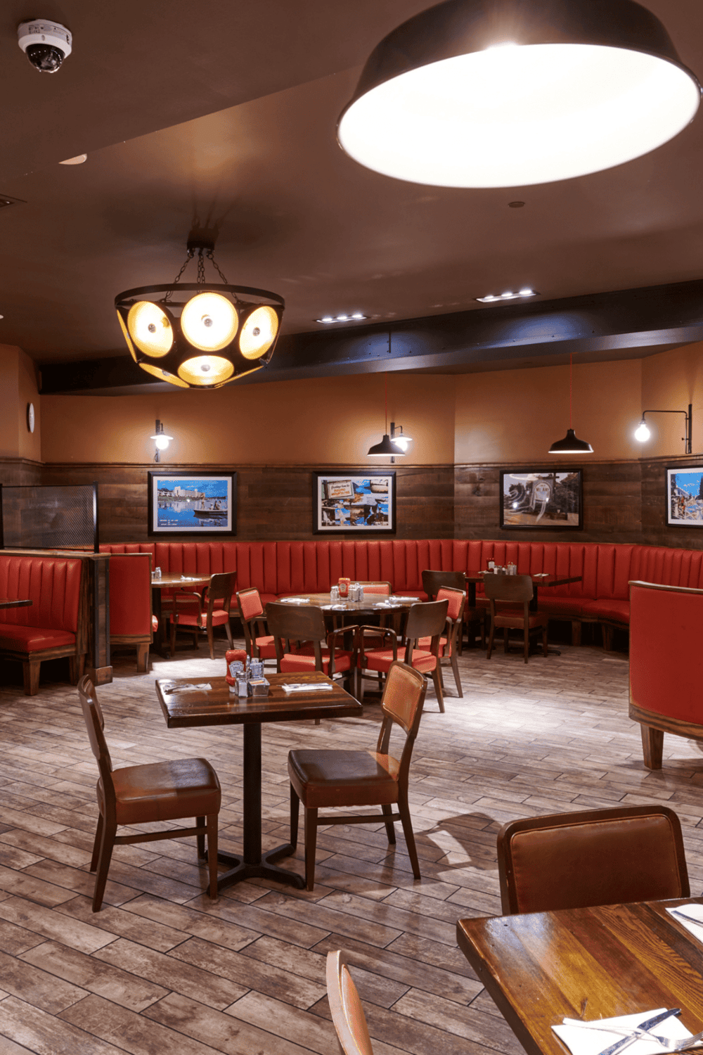 Indoor restaurant dining area with red upholstered booths and wooden tables, warm ambient lighting.