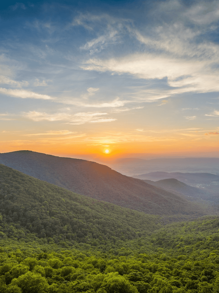 Sunset over lush green mountains with vibrant sky and scenic landscape.