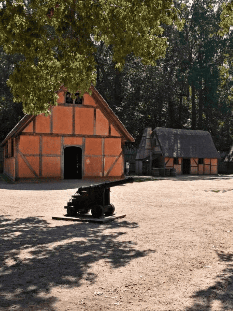 Ancient cannon outside historic German village replica with traditional timber-framed houses.