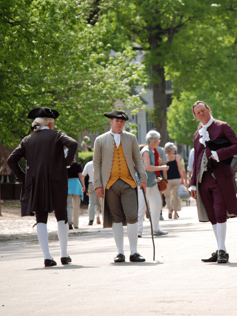 Historians dressed in 18th-century clothing at a historical reenactment in a park setting.