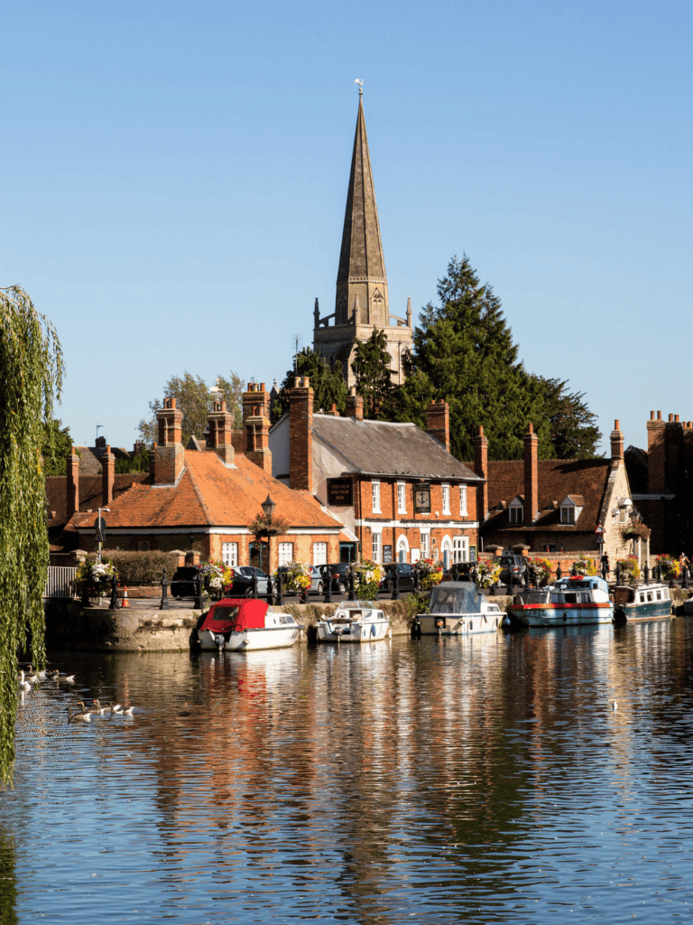 Charming riverside village with historic buildings, boats, and a church steeple in a scenic town in England.