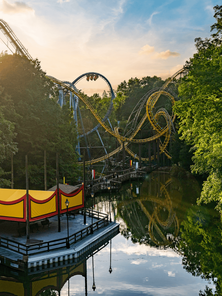 Thrilling roller coaster ride at Quest For Directions amusement park, surrounded by lush greenery and scenic water reflections.