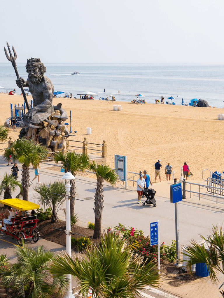 Statue of Neptune on a sunny beach with palm trees and beachgoers enjoying the seaside scenery.
