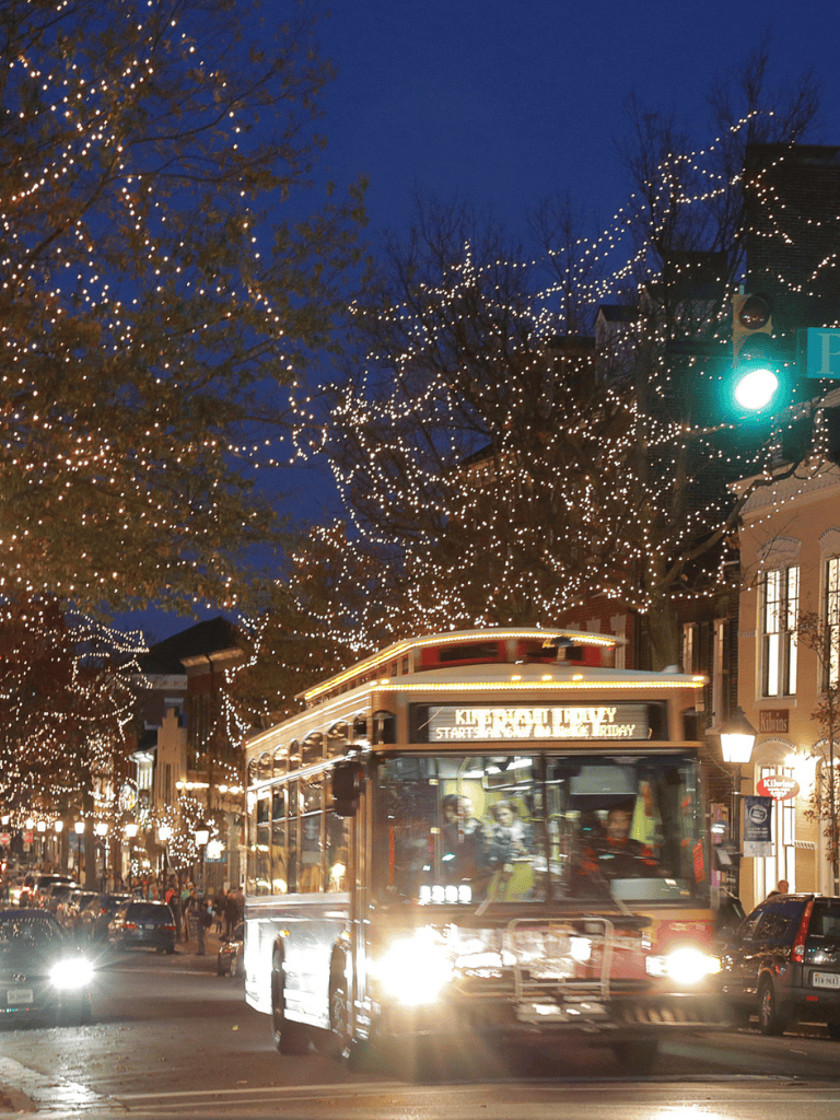 Bright streetcar on busy downtown street during holiday season, illuminated by festive lights.