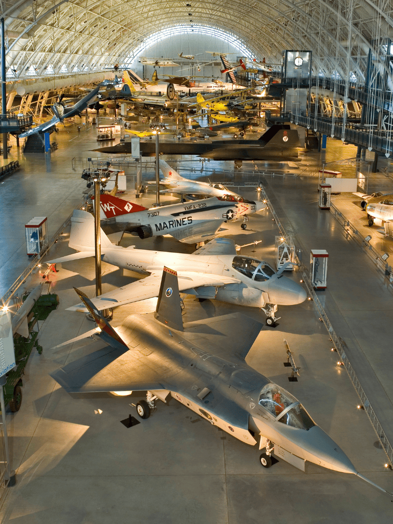 Fighter jets and military aircraft displayed in a spacious aviation museum hangar.