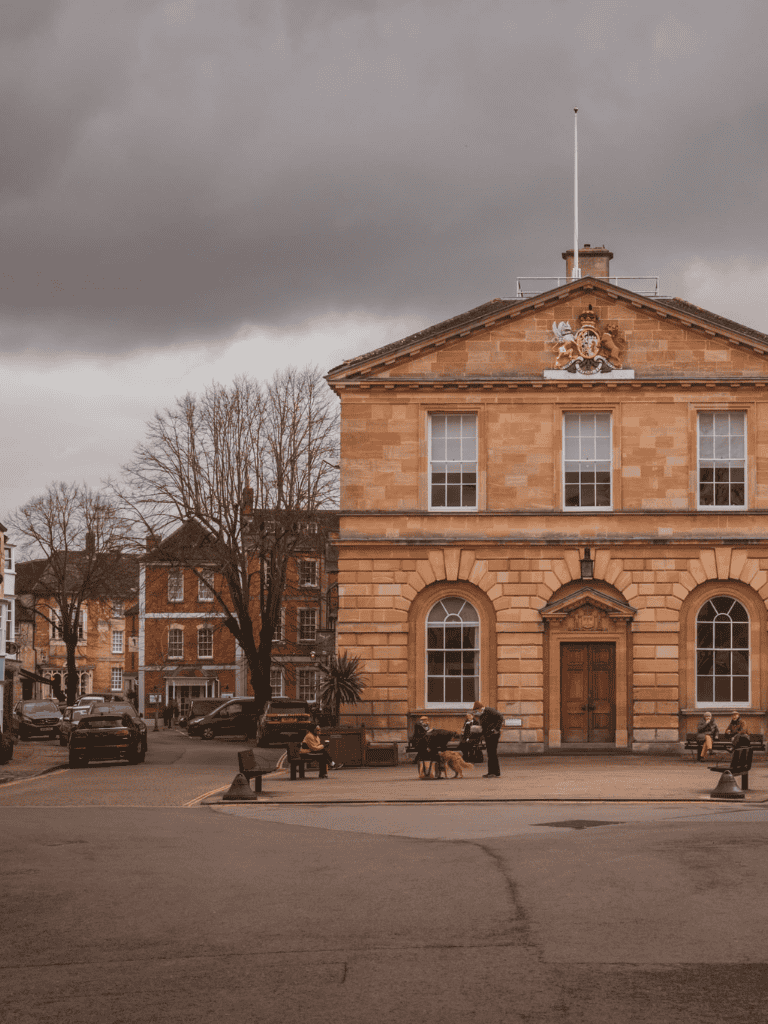 Historic town hall building with people sitting on benches and overcast sky, showcasing urban scenery and architecture.