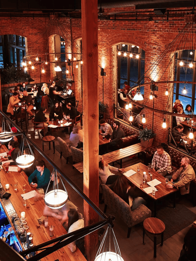 Cozy brick-walled restaurant with warm ambient lighting and diverse groups of people dining.