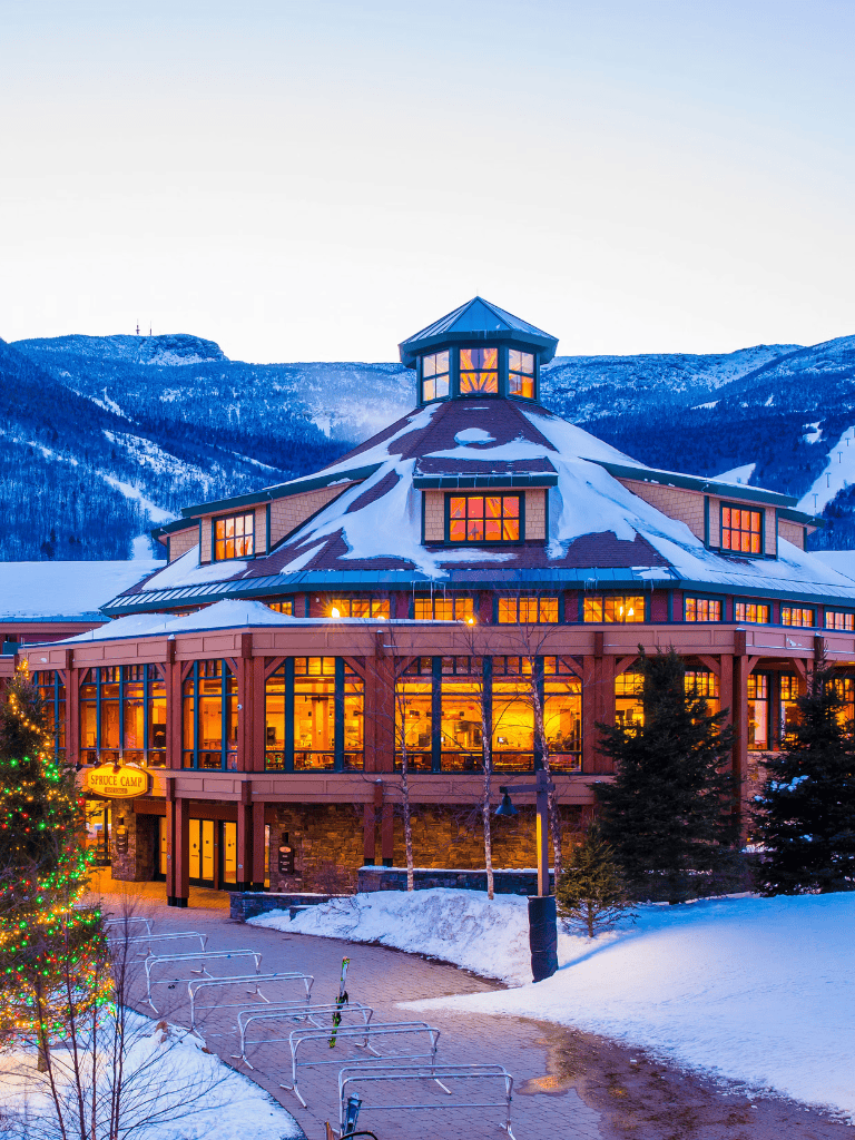 Cozy mountain lodge during winter with snow-covered landscape and warm-lit interior.