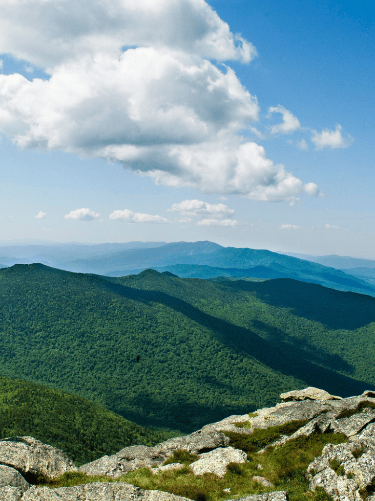 Vast green mountain landscape with blue sky and clouds, scenic view for outdoor adventure travel.