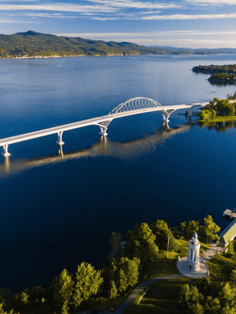 Aerial view of the scenic Quest for Directions bridge over a large lake with lush green hills in the background.