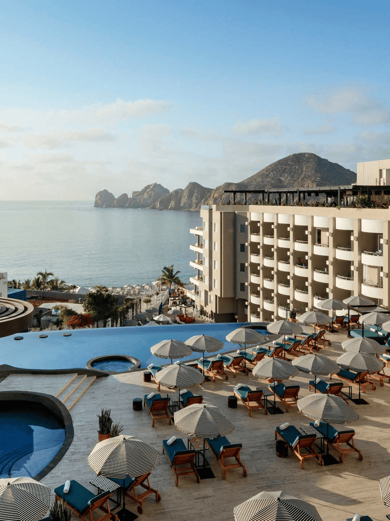 Relaxing poolside view at Quest for Directions hotel with ocean and mountain backdrop in Cabo San Lucas, Mexico.