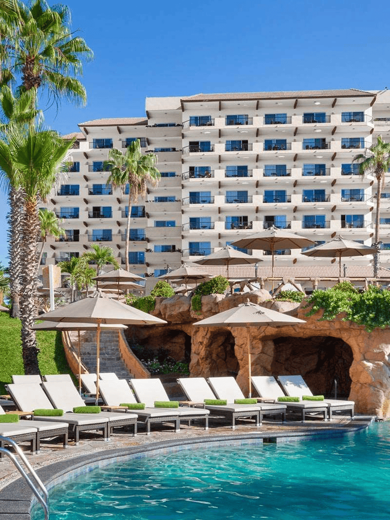 Luxurious resort pool with palm trees and modern hotel in the background, ideal vacation destination.