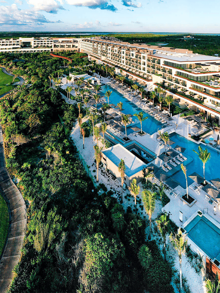 Luxurious tropical resort with pools, palm trees, modern hotel, and lush landscaped gardens.