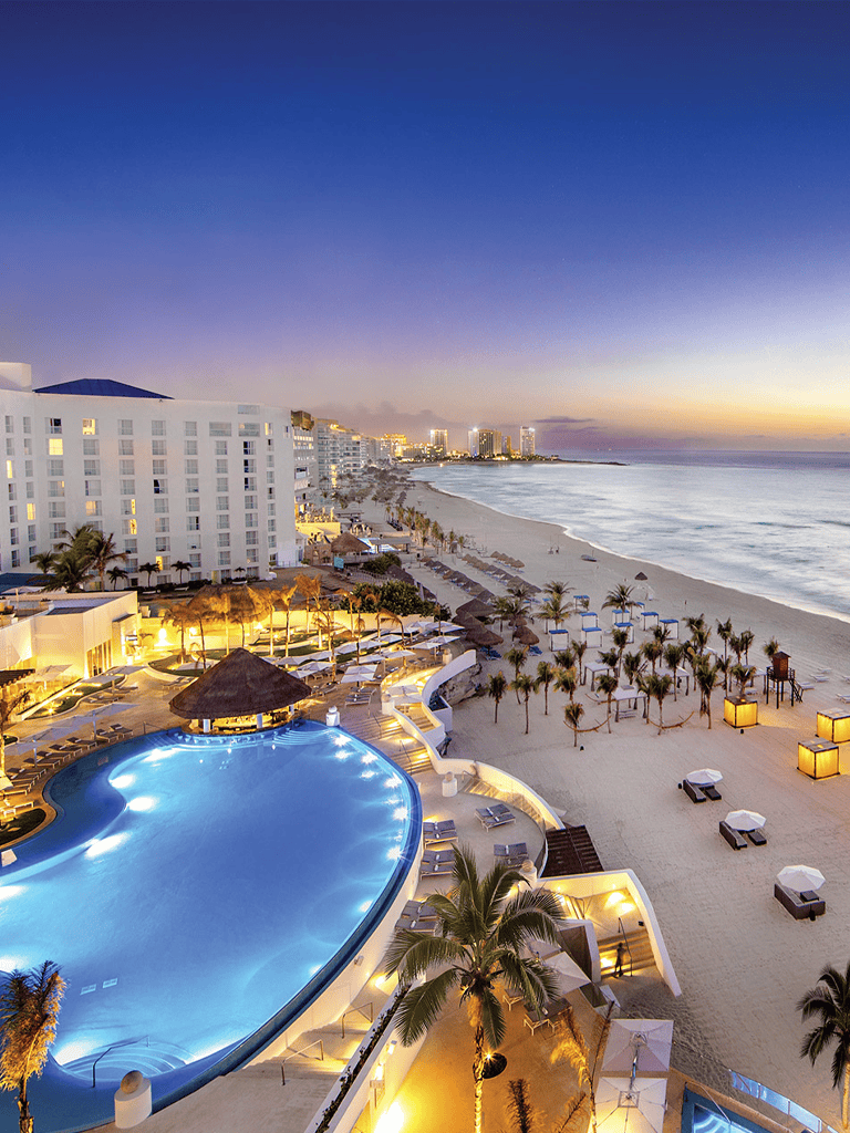 Stunning beachside resort at sunset with pool, palm trees, and ocean view in Cancun, Mexico.