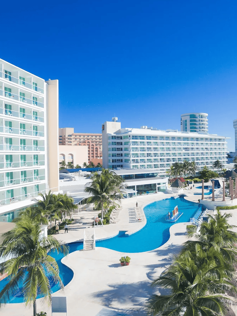 Outdoor luxury hotel pool with palm trees and modern high-rise buildings in the background.