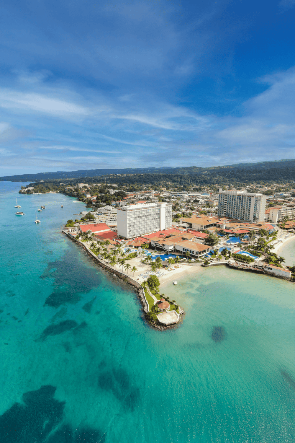 Stunning aerial view of a coastal resort with turquoise waters, sandy beaches, and lush greenery.