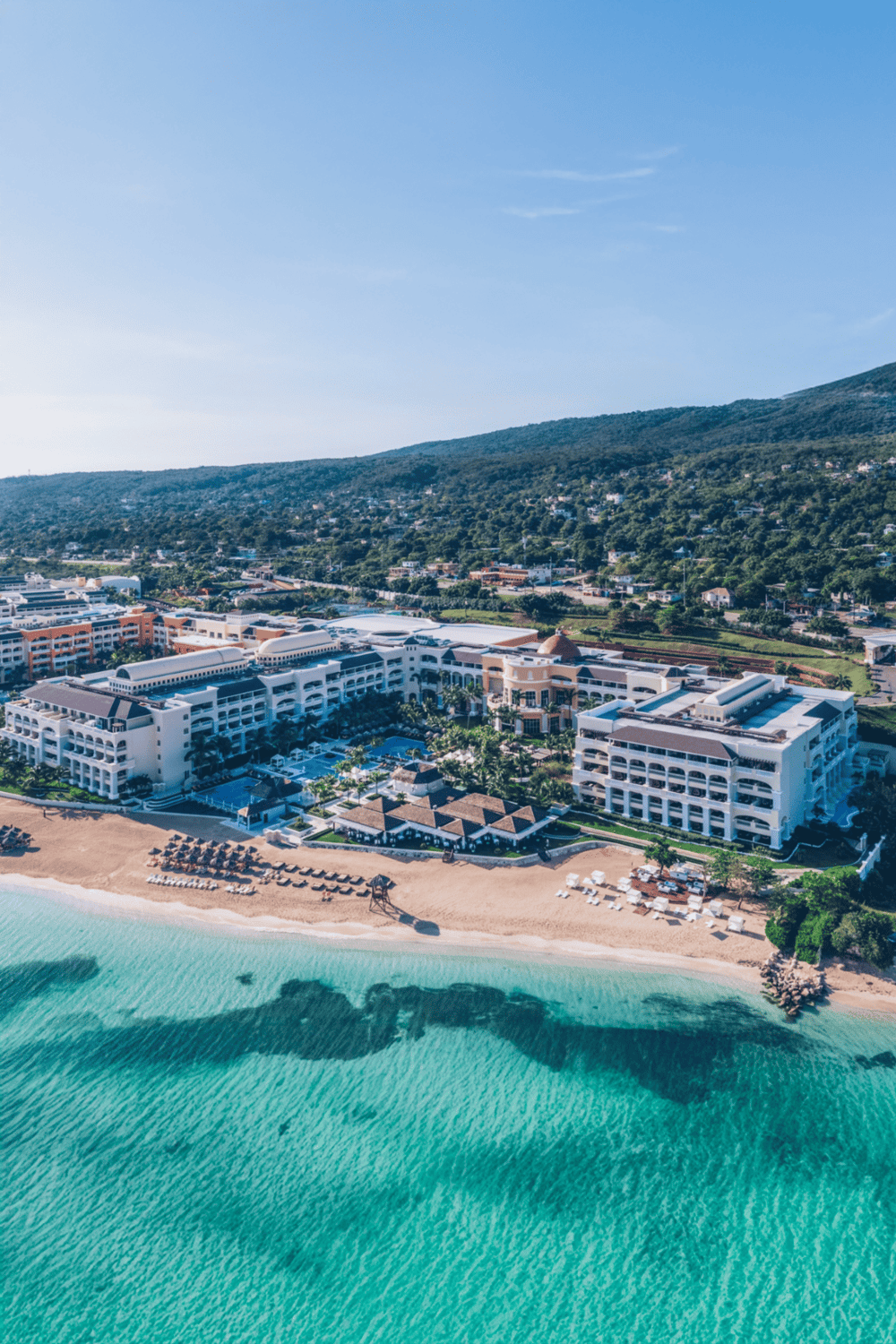 Luxury beachfront resort with scenic ocean views and lush green mountains in the background.