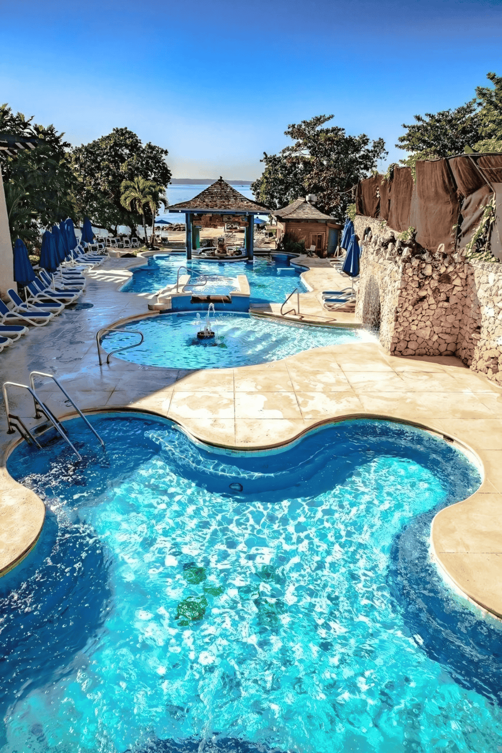 Relaxing outdoor pool and hot tub with scenic ocean view, lush greenery, and poolside amenities.