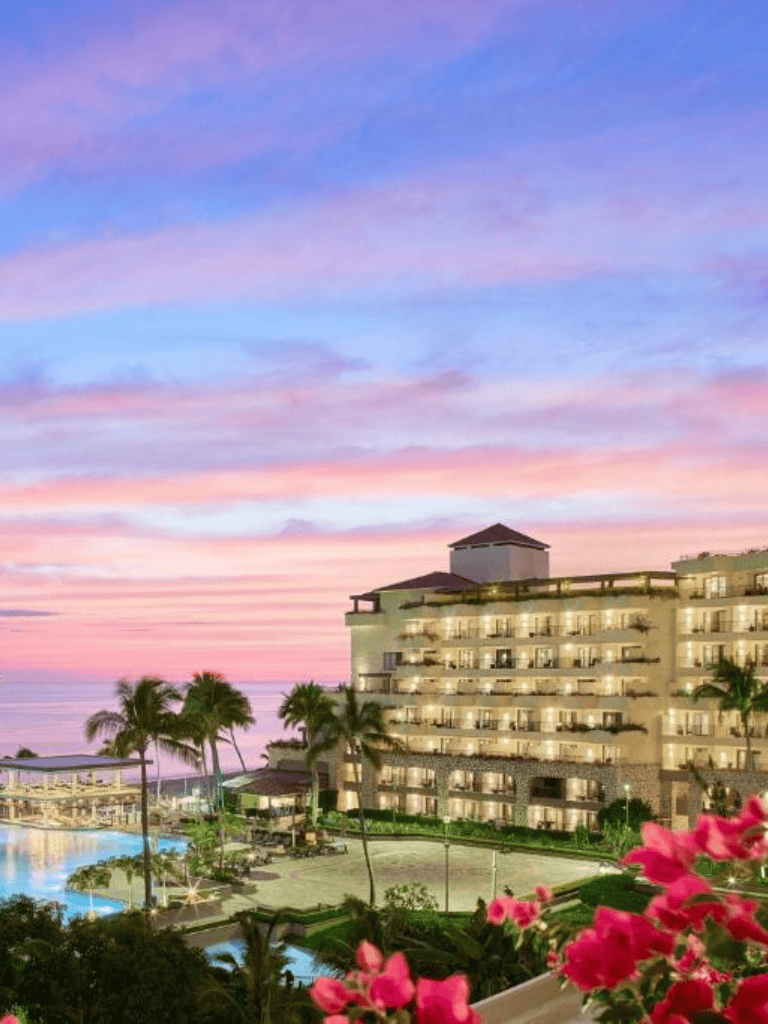 Luxurious beach resort at sunset with palm trees and pink flowers, perfect for vacation getaways.