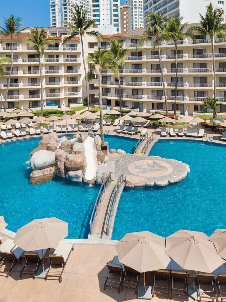 Pool with waterfalls and surrounding lounge chairs at a luxury hotel.