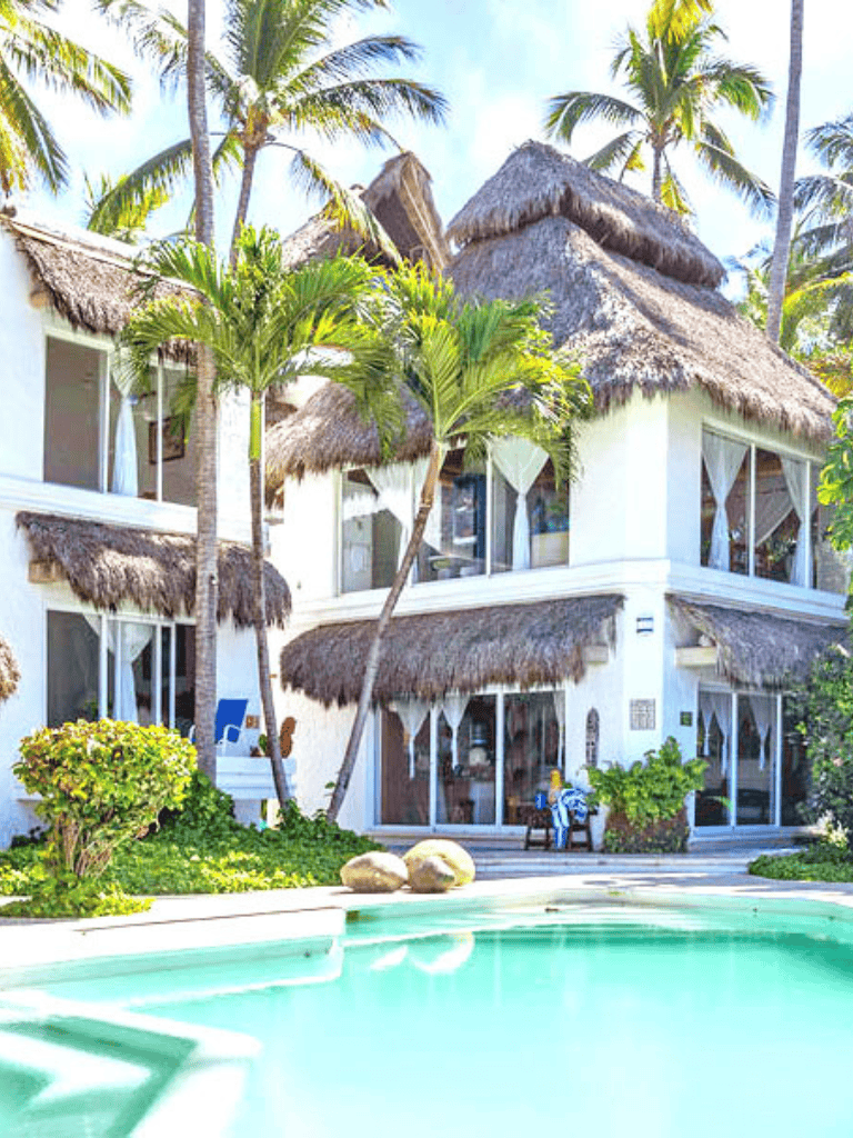 Luxurious tropical villa with pool and thatched roofs, surrounded by palm trees and lush greenery.