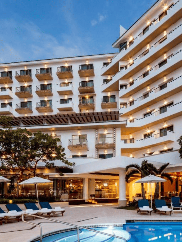 Luxurious hotel with balconies, pool, and outdoor lounge area at sunset.