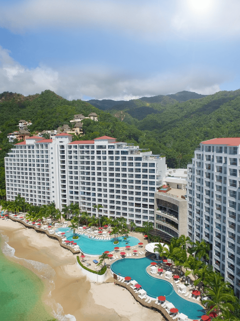 Luxurious beachfront resort with pools, overlooking the ocean and lush green mountains, perfect for vacation stays.
