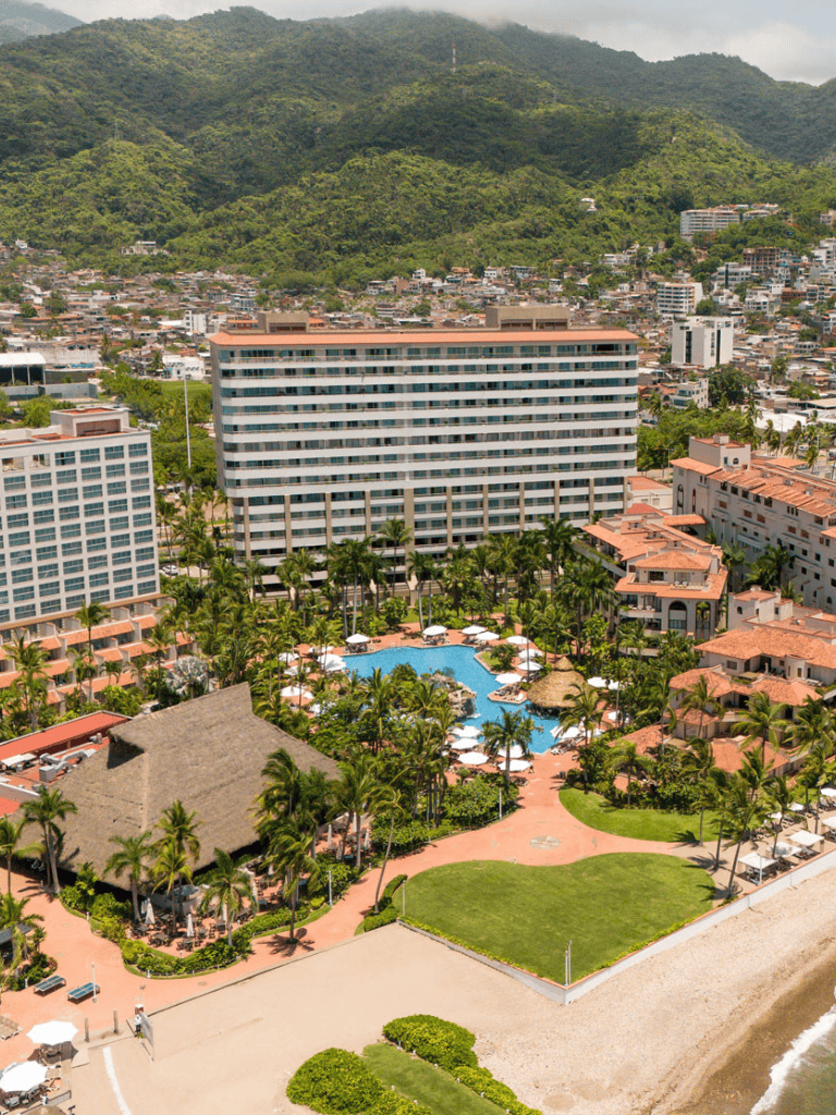 Luxurious beachfront resort with pool overlooking ocean and lush mountains in the background.