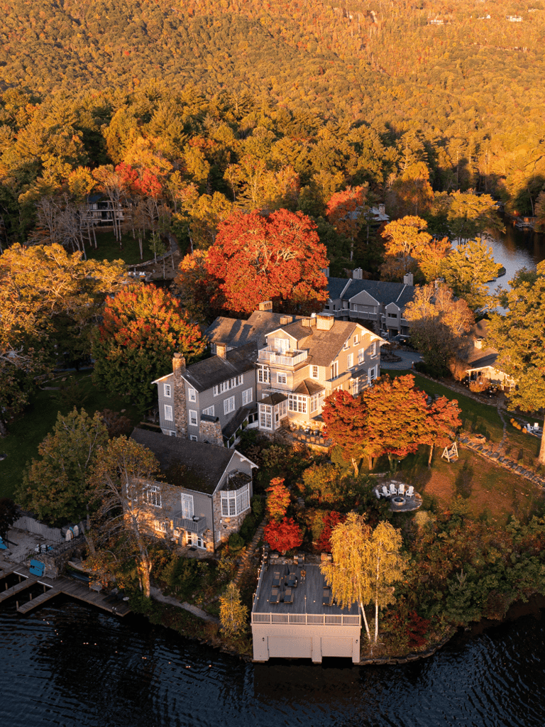Luxurious lakeside mansion in vibrant fall foliage with outdoor deck and scenic views.