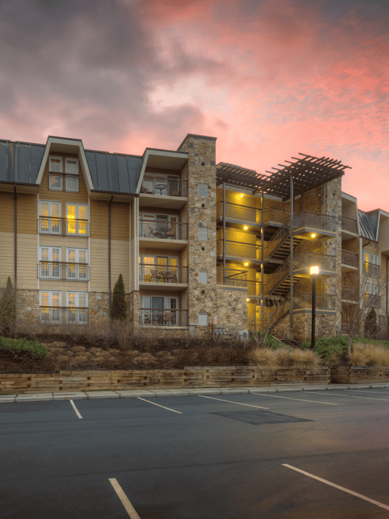 Modern multi-story apartment building with exterior lighting at sunset, in a scenic mountain setting.