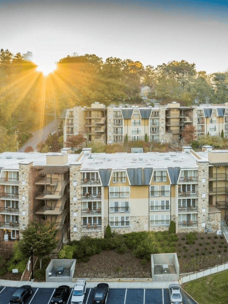 Modern apartment complex with scenic hillside views at sunset, featuring multiple stories and landscaped grounds.