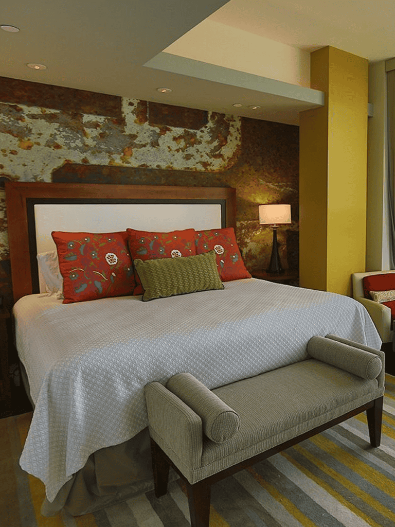 Cozy hotel bedroom with decorative pillows, textured wall, and modern decor.