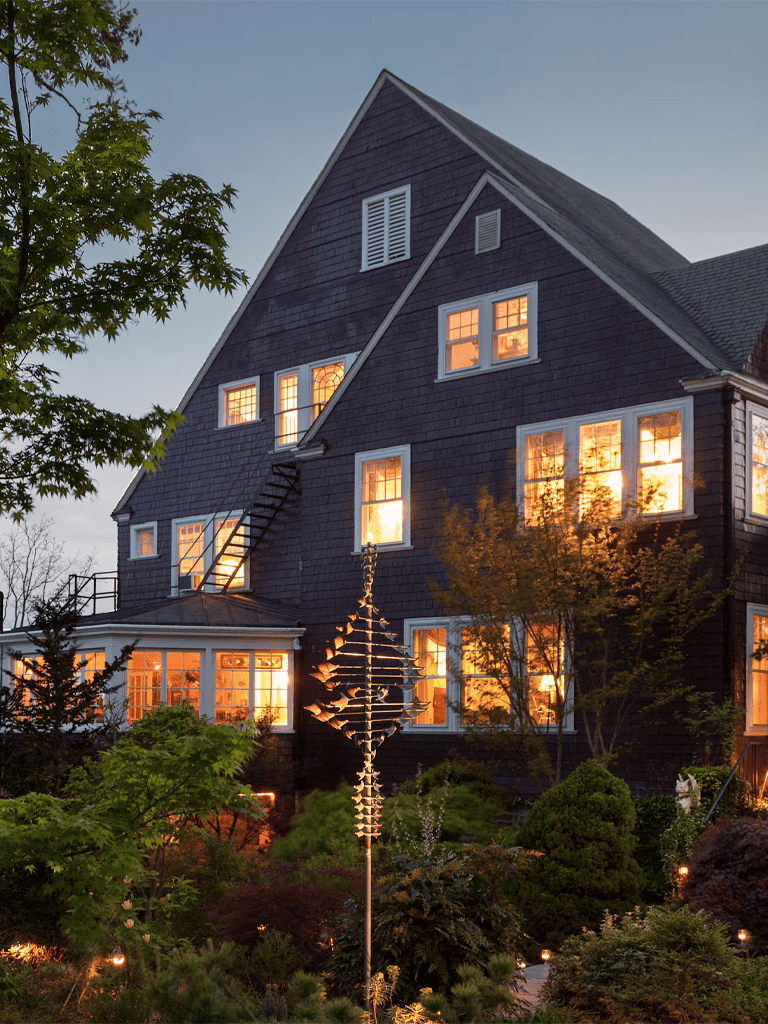 Charming dark blue house with illuminated windows and lush garden at dusk.