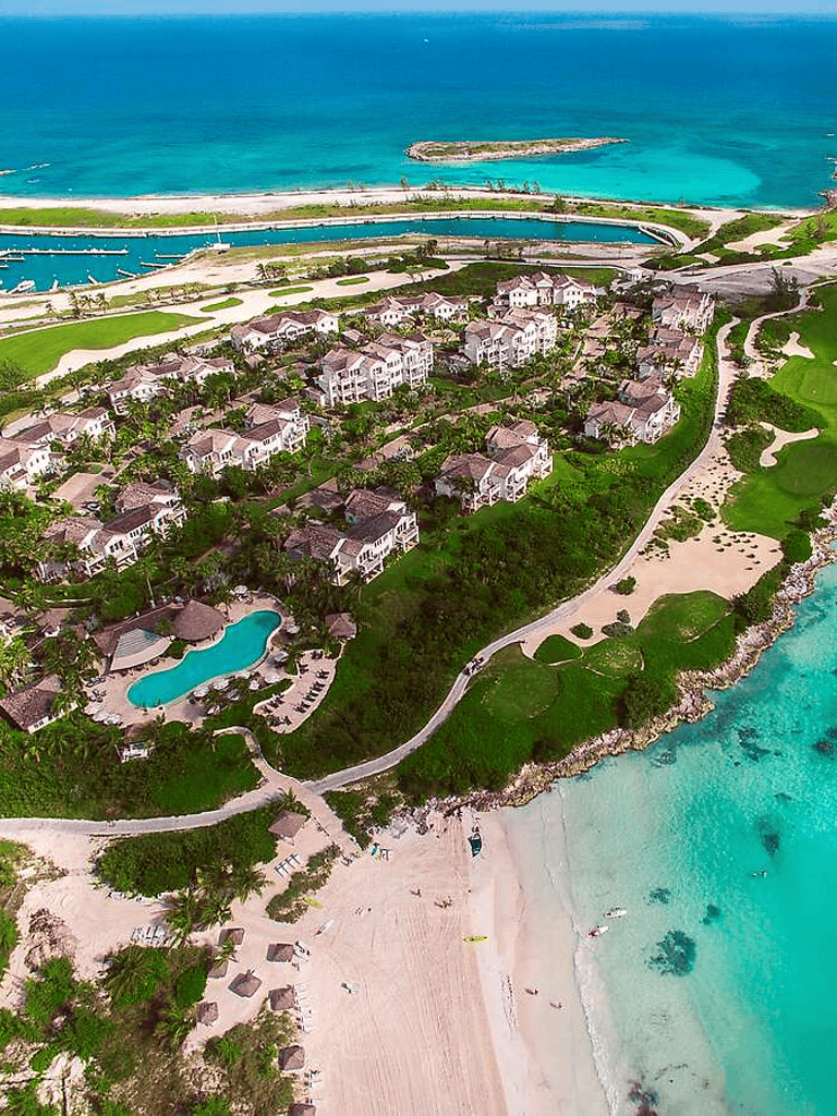 Aerial view of beachfront resort with swimming pool, lush greenery, and ocean coastline.