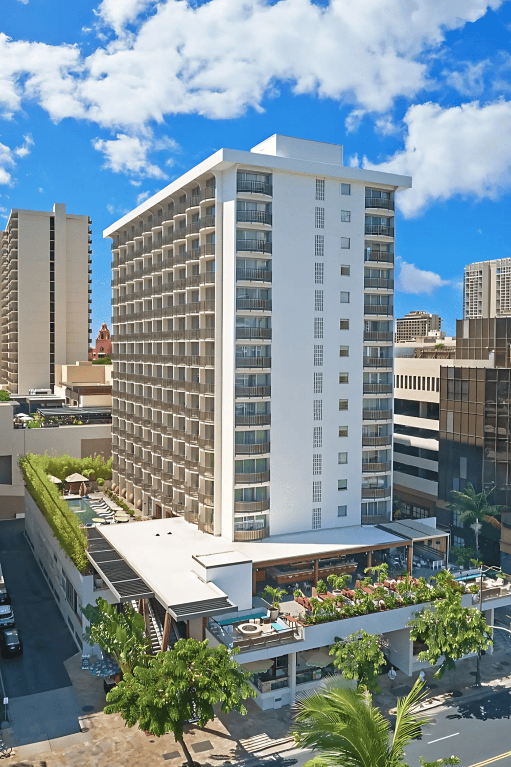 Modern high-rise hotel building in downtown cityscape with rooftop pool and lush outdoor lounge area.