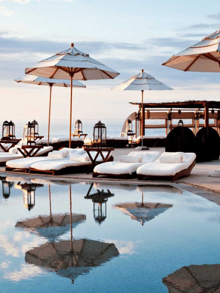 Beachside resort with umbrellas and lounge chairs by the pool.