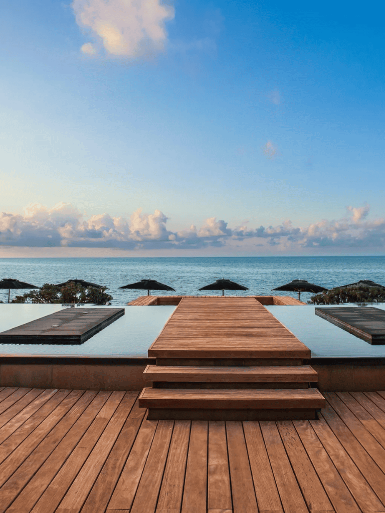 Relaxing oceanfront pool with wooden deck and beach umbrellas, perfect for vacation relaxation.