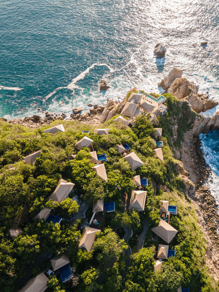 Luxurious oceanfront resort with private pools and lush greenery on rocky coastline.