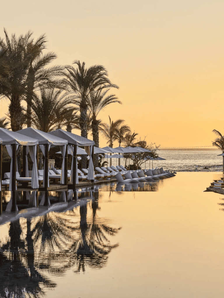 Palms and cabanas over infinity pool at sunset, tropical beach resort relaxation.