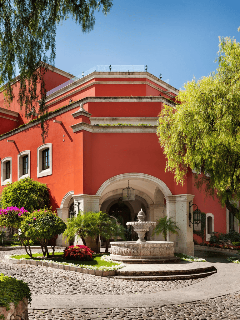 Elegant red building with lush landscaping and fountain, perfect for travel inspiration.