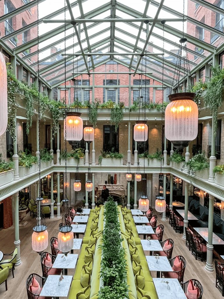 Bright indoor garden restaurant with glass ceiling, hanging lanterns, and lush greenery for elegant dining experience.