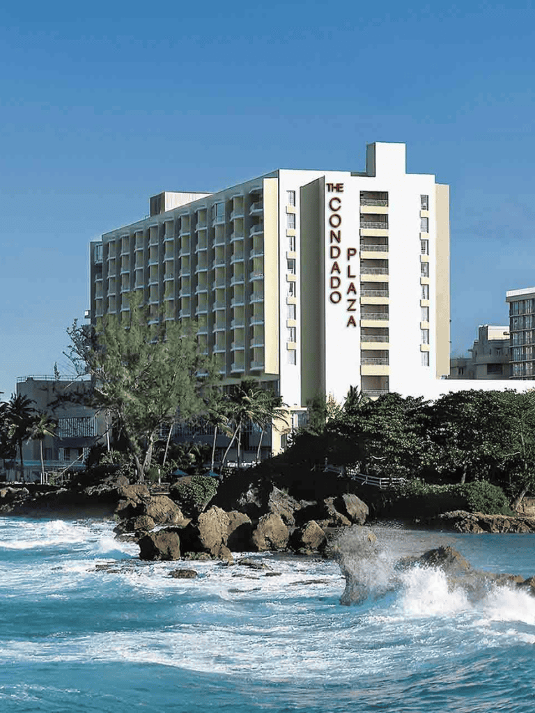 Modern hotel building near the ocean on a sunny day with the Quest for Directions logo.