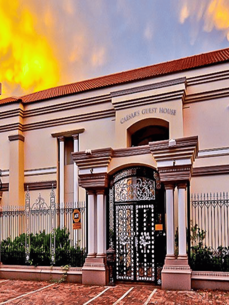 Charming Caesar Guest House with elegant gate and inviting exterior in a warm sunset ambiance.